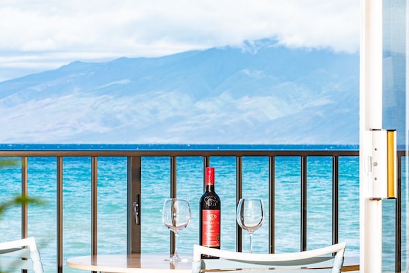 A table with a bottle of wine and two glasses, overlooking a body of water with mountains in the background.