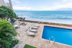 A pool area with lounge chairs and a view of the ocean.