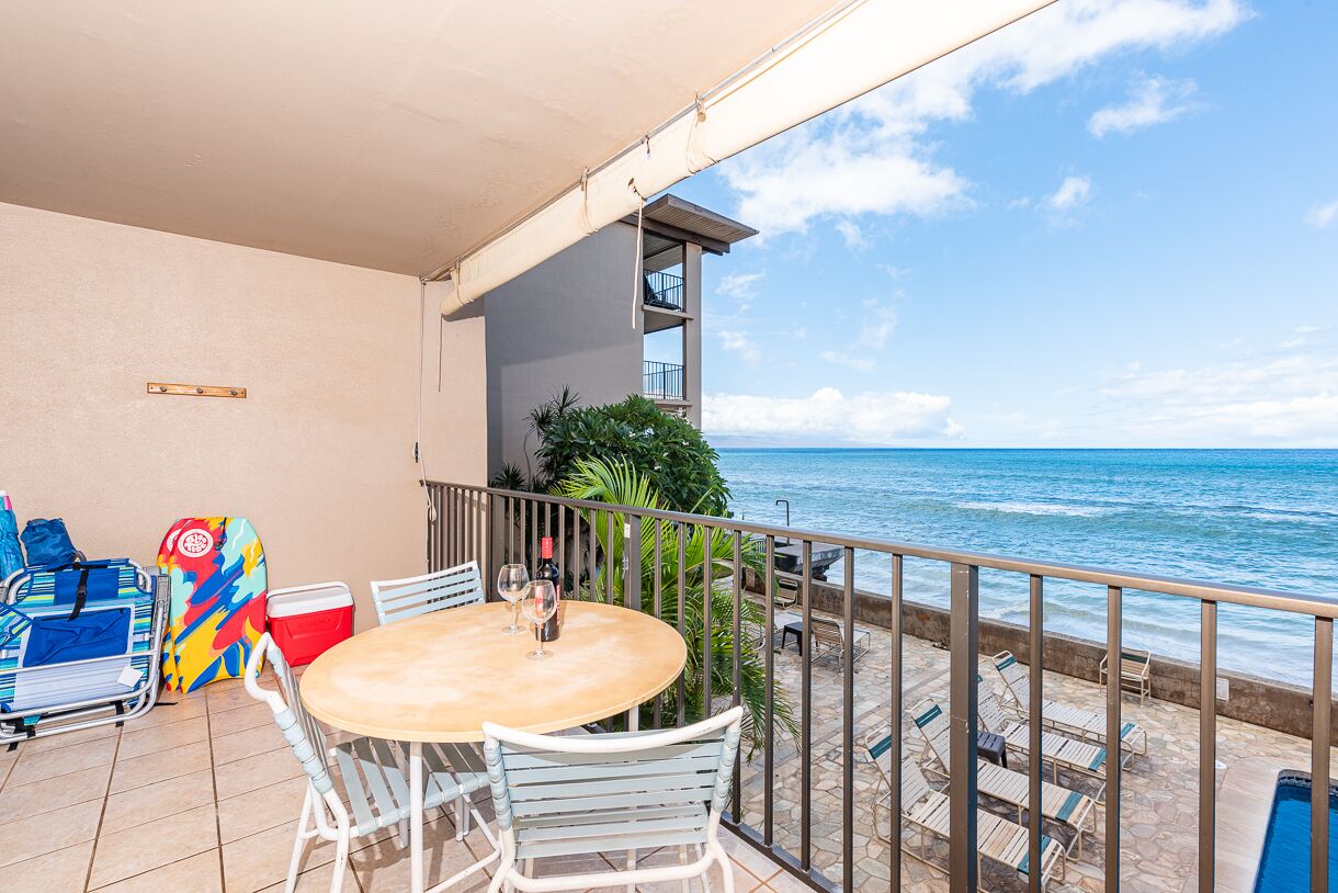 A balcony with a table and chairs, a view of the ocean, and a pool.