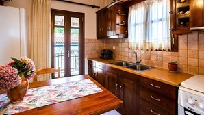Una cocina con armarios de madera, un fregadero y una estufa. Hay una ventana con cortinas, un jarrón con flores sobre la mesa y un salpicadero de azulejos.