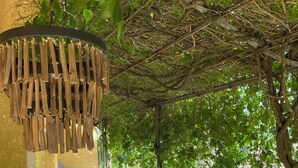 Ein überdachter Außenbereich mit Holztisch und -stühlen, umgeben von einem Metallzaun und üppigem Grün.