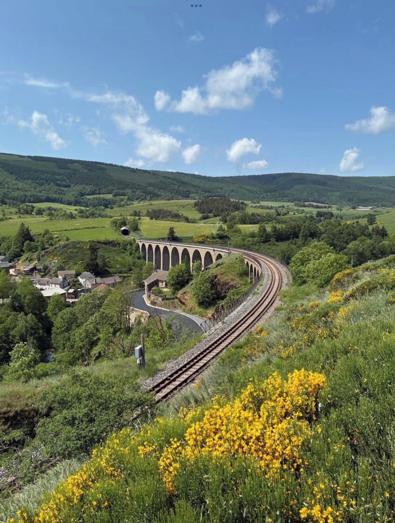 A railway track curving through a green landscape with a viaduct over a valley.