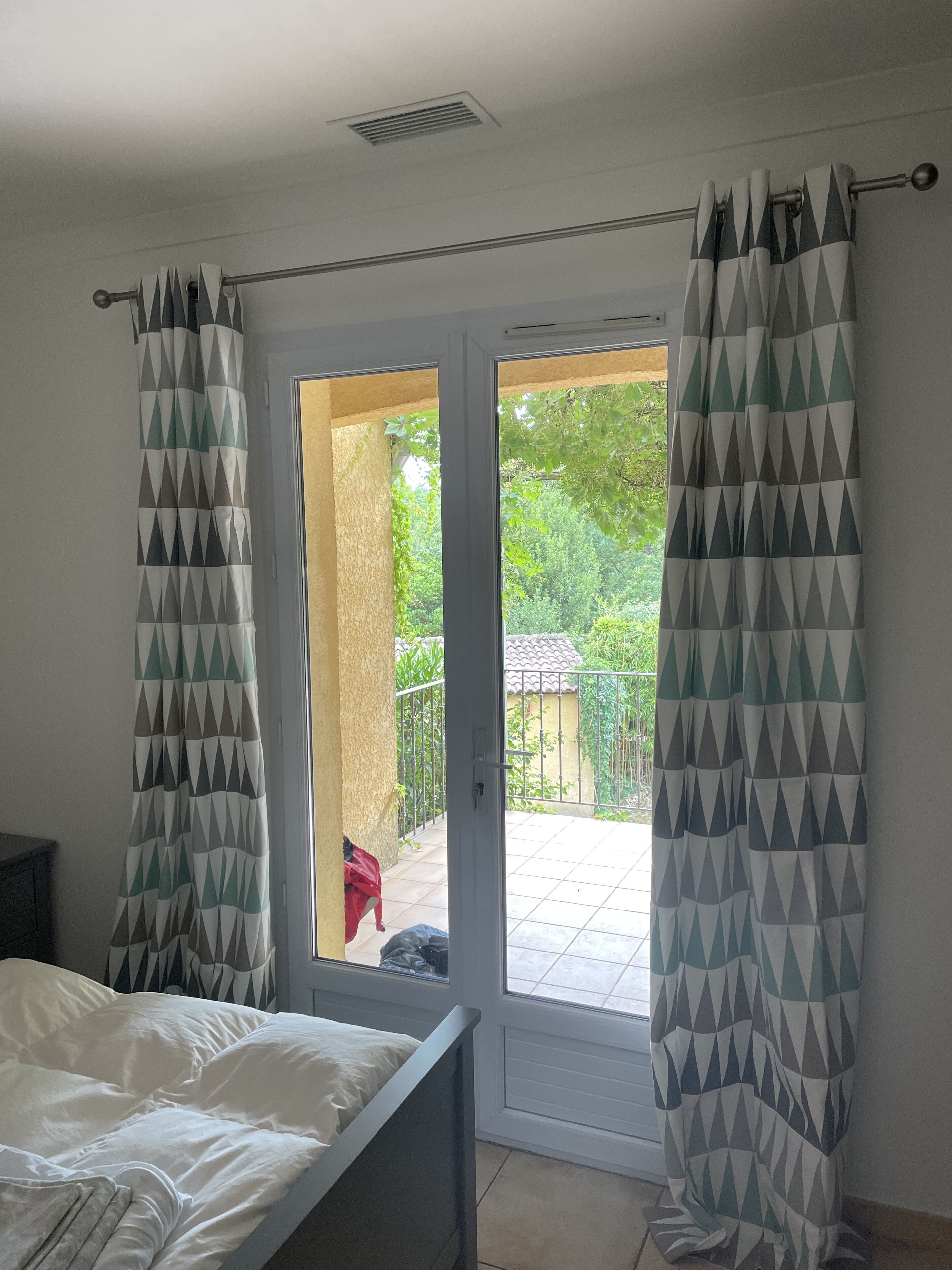 A bedroom with a bed, a sliding glass door leading to an outdoor area with a tiled patio and greenery.