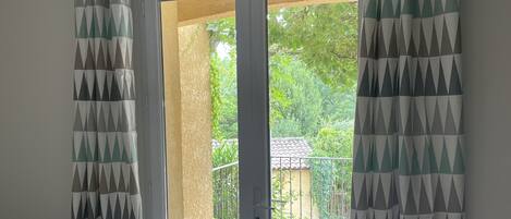 A bedroom with a bed, a sliding glass door leading to an outdoor area with a tiled patio and greenery.