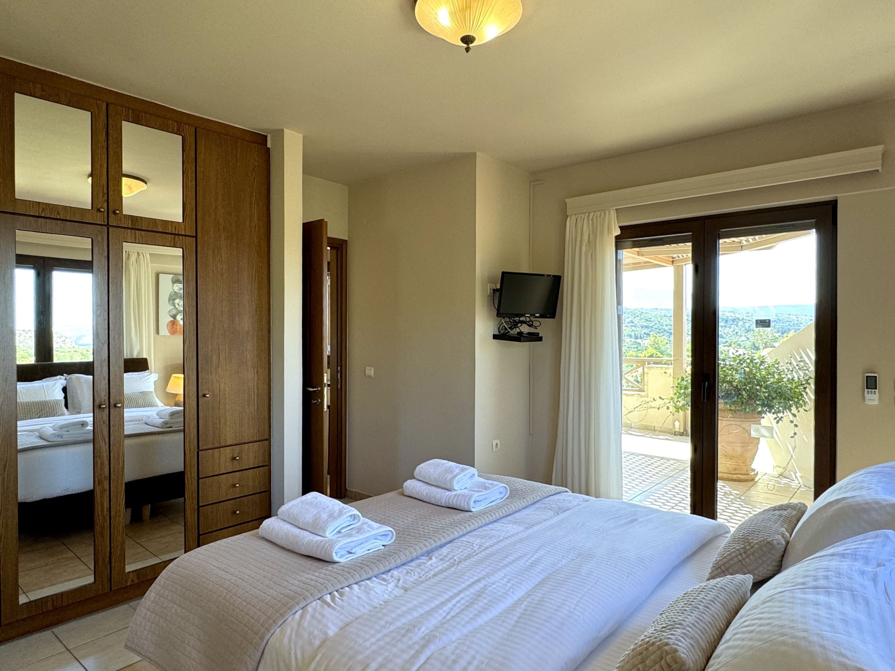 Une chambre d’hôtel avec un grand lit, un téléviseur fixé au mur et une porte-fenêtre coulissante donnant sur un balcon.