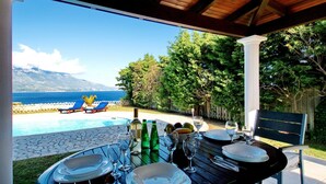 An outdoor dining area with a view of the sea and mountains, equipped with tables, chairs, and a pool. - Villa Afroditi in Spartia (Kefalonia)