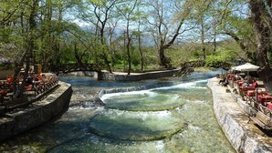 A riverside restaurant with outdoor seating and a stone bridge. - Villa Artemis in Vrises (Apokoronas)