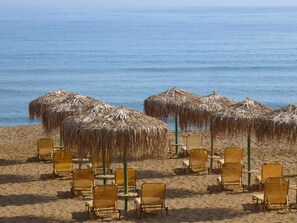 A beach with rows of sun loungers and thatched umbrellas. - Rouladina Apt 2 in Stalos (Chania)