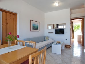 Cozy living space with a dining area and seating area, featuring a dining table, chairs, and a sofa with a flat-screen TV above.