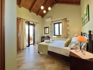 A bedroom with two beds, a wooden ceiling, a balcony, and a view of the outdoors. - Villa Afrati in Plaka (Apokoronas)