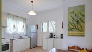 Een keuken met witte kastjes, een roestvrijstalen koelkast, een fornuis, een koffiezetapparaat en een fruitmand op tafel.
