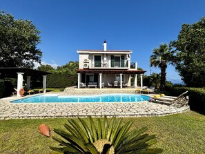 A two-story house with a swimming pool, outdoor furniture, and a garden.