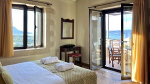 A hotel room with a bed, a desk, a chair, and a sliding glass door leading to an outdoor area with a view of the sea. - Villa Zara in Plaka With 3 Bedrooms and 3 Bathrooms (Apokoronas)