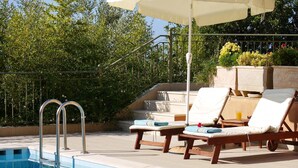 Un espace aménagé au bord de la piscine, avec des chaises longues, une piscine et un escalier menant à un niveau supérieur.