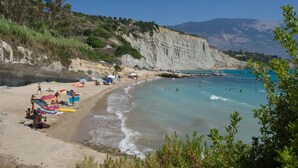 A beach with clear turquoise waters, a sandy shore, and cliffs in the background. - Villa Odysseus in Spartia (Kefalonia)