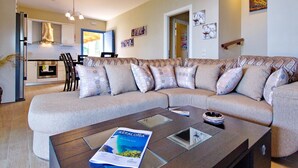 A modern living room with a sectional sofa, a coffee table with a magazine, and a kitchen in the background. - Villa Odysseus in Spartia (Kefalonia)
