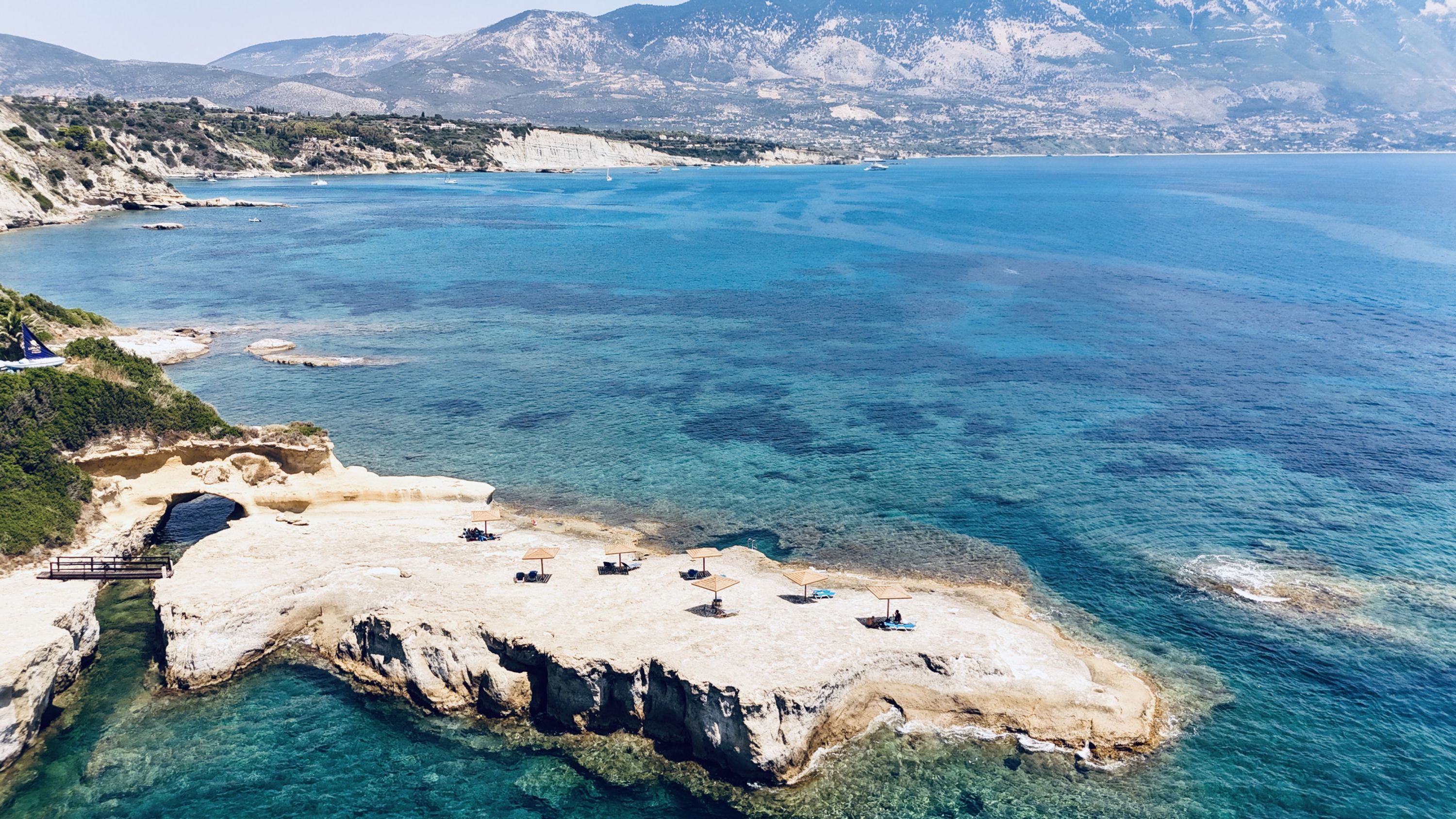 Zona costera con aguas azul turquesa, terreno rocoso y una pequeña playa con sombrillas.