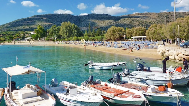 A coastal marina with several boats docked, a sandy beach with umbrellas, and a backdrop of hills. - Villa Anemi in Sternes (Chania)