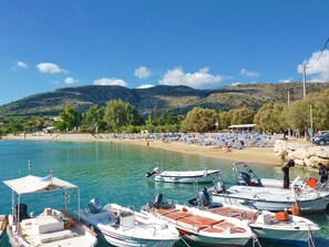 A coastal marina with several boats docked, a sandy beach with umbrellas, and a backdrop of hills. - Villa Anemi in Sternes (Chania)