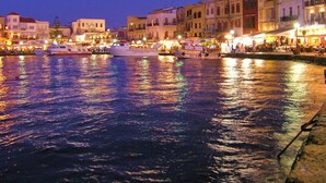 A waterfront area with boats docked, buildings with balconies, and a waterfront promenade with people. - Villa Anemi in Sternes (Chania)