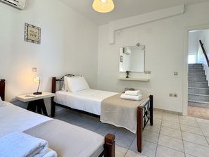A hotel room with two beds, a bedside table with a lamp, a mirror, a small shelf with a plant, and a staircase leading to another floor.