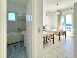 A bathroom with a bathtub and a shower, a bedroom with a bed and a balcony.
