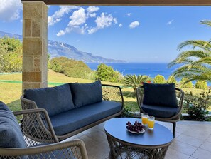 A covered outdoor seating area with a view of the sea and mountains.