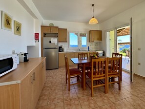 A kitchen with wooden cabinets, a stainless steel refrigerator, a dining table with chairs, and a view of the outdoors through a glass door.