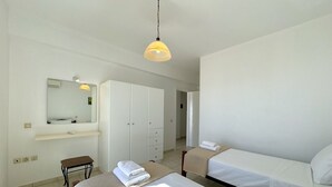 Habitación de hotel con cama, mesita de noche, silla, armario, espejo y lámpara colgante.