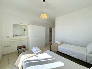 A hotel room with a bed, a bedside table, a chair, a wardrobe, a mirror, and a hanging light fixture.