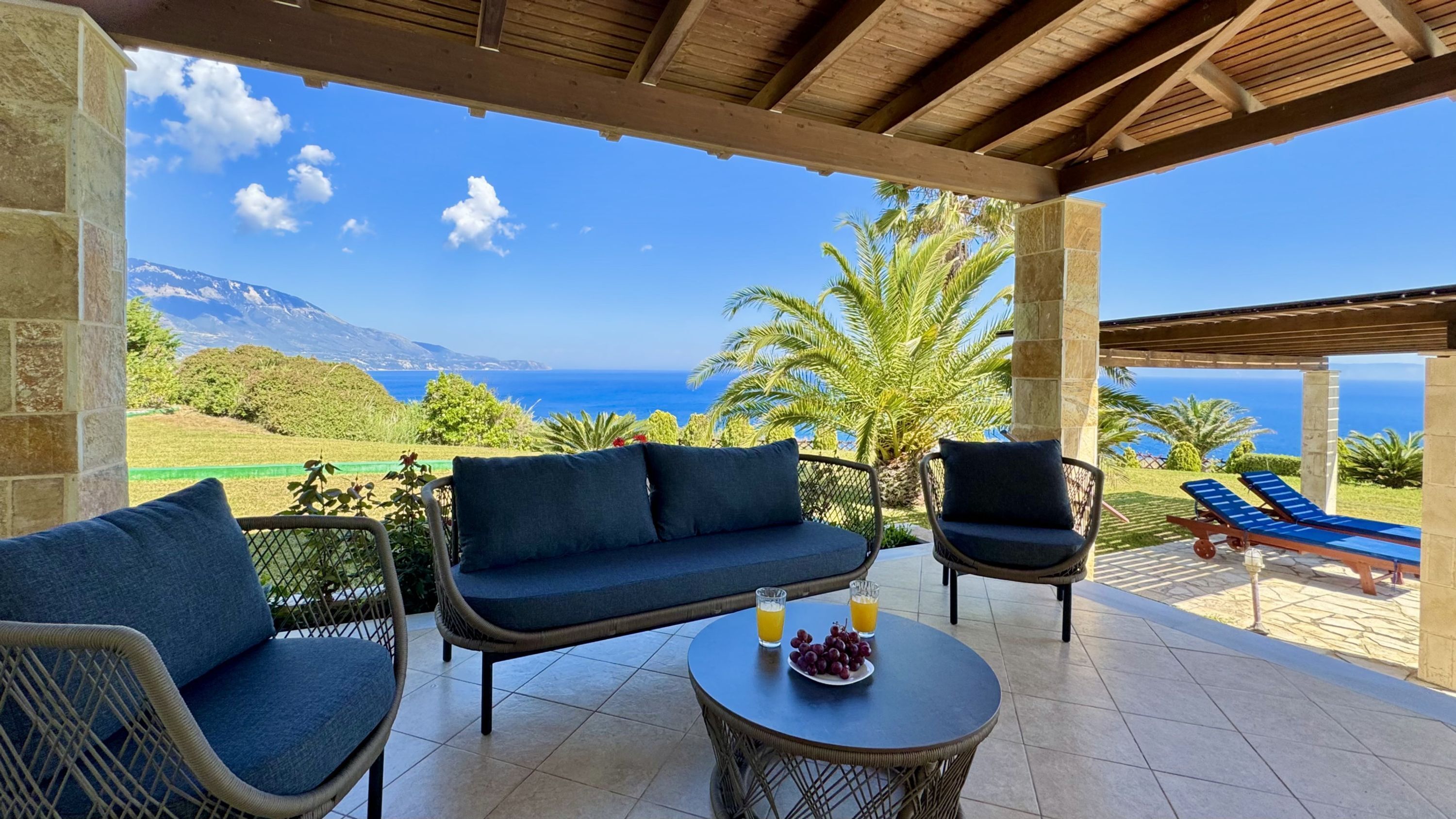 A covered outdoor seating area with a view of the sea and mountains.