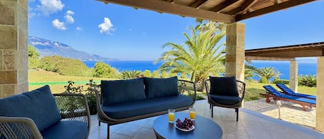 A covered outdoor seating area with a view of the sea and mountains.