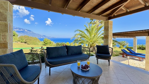 A covered outdoor seating area with a view of the sea and mountains.