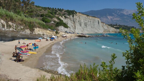 Une plage à l’eau turquoise et limpide, avec un rivage sablonneux et des falaises en arrière-plan.