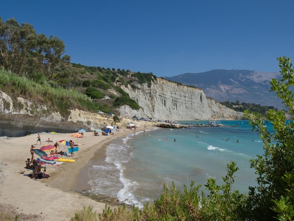 A beach with clear turquoise water, sandy shore, and cliffs in the background.