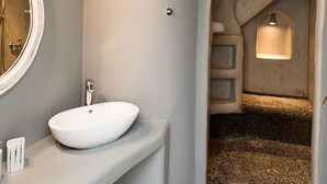 Un baño moderno con tocador curvo, espejo redondo y zona de ducha integrada con pared de piedra.