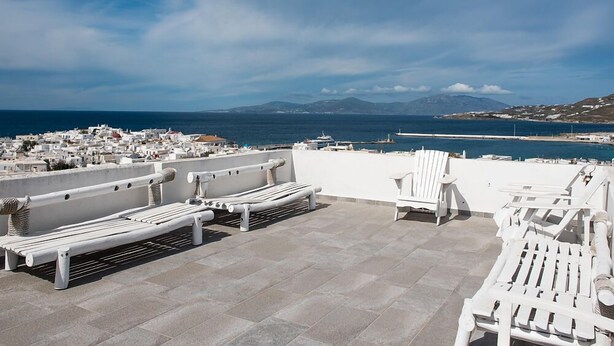 Terraza en la azotea con sillones blancos y vistas al mar y montañas distantes.