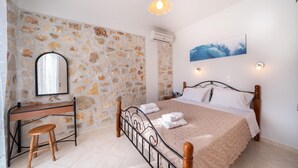 A bedroom with a stone wall, a bed with a wooden headboard, a desk with a mirror, and a hanging light fixture. - Villa Mounda Poseidon (Kefalonia)