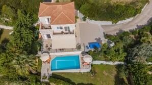 An aerial view of a house with a swimming pool, surrounded by lush greenery and a paved driveway. - Villa Mounda Poseidon (Kefalonia)
