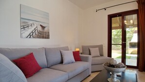 Ein modernes Wohnzimmer mit einem grauen Sofa, roten Kissen, einem Couchtisch mit einer dekorativen Schale und einem Gemälde, das eine Küstenlandschaft zeigt.