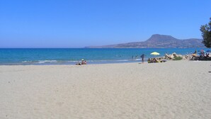 A beach with clear skies, calm waters, and a mountain in the background.