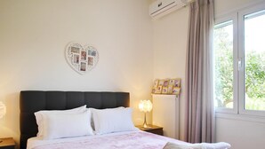 Una cama bien hecha con ropa de cama blanca y rosa, un collage de fotos con forma de corazón en la pared y una ventana con cortinas.