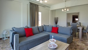 Una sala de estar moderna con un sofá seccional gris, cojines rojos, una mesa de centro de madera y un comedor al fondo.