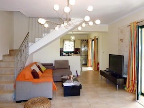 A living room with a sofa, coffee table, TV, and a staircase leading to a kitchen.