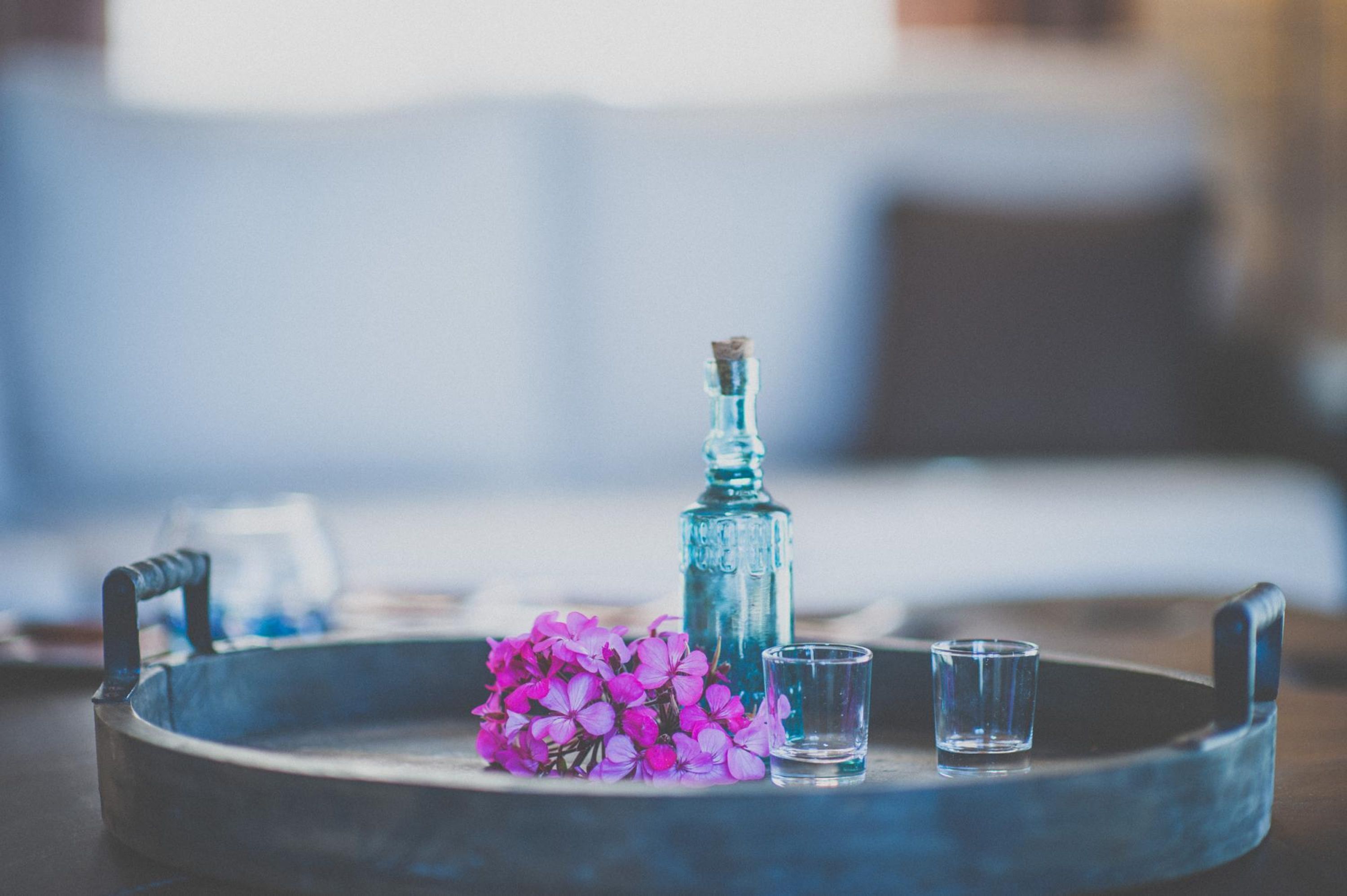 A tray with a bottle, flowers, and shot glasses on a table.