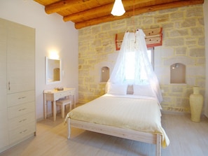 Une chambre avec un mur en pierre, un lit à baldaquin, un plafond en bois et une table de chevet.