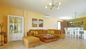 A living room with a sectional sofa, a glass display cabinet, and a dining area with white chairs and a table. - Villa Alexandros in Spartia (Kefalonia)