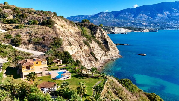 A coastal property with a swimming pool, a patio area, and a view of the sea and mountains.