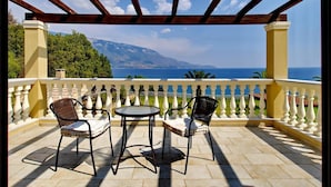 A covered outdoor seating area with two chairs and a table, overlooking a scenic view of the sea and mountains. - Villa Alexandros in Spartia (Kefalonia)
