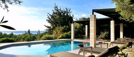 A poolside area with lounge chairs, a table with a drink, and a view of the sea.